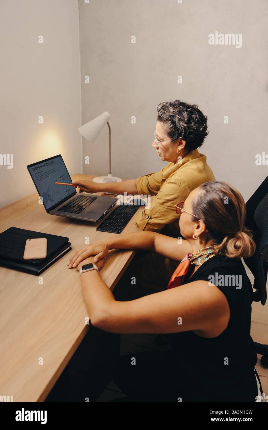 Two mature professionals collaborate on a project, discussing and analyzing data shared on a laptop. Stock Photo