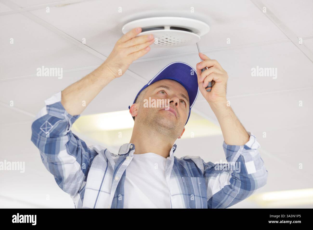 electrician installing smoke detector on ceiling Stock Photo