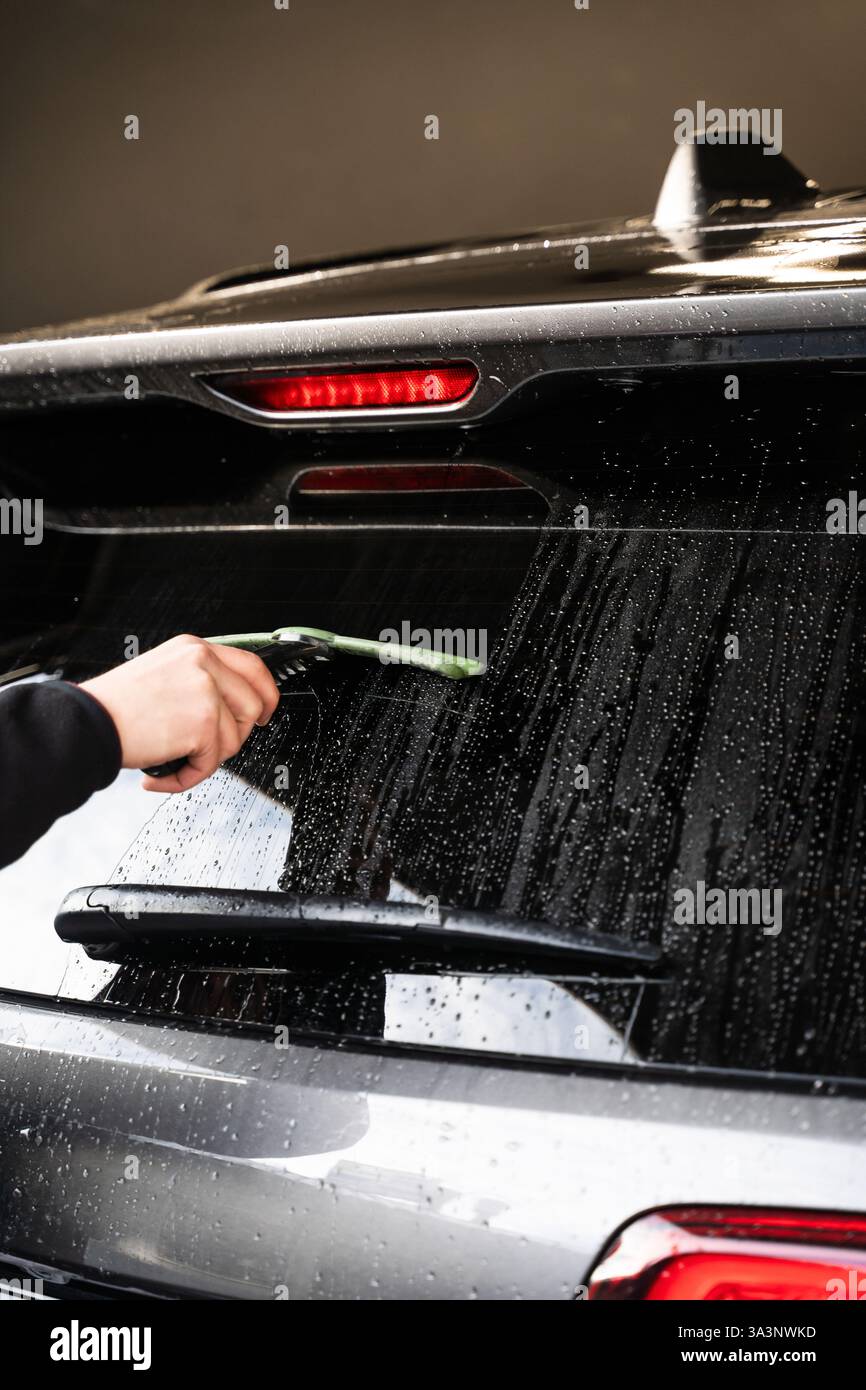 Removing water from glass surface of car using squeegee. Cleaning rear ...