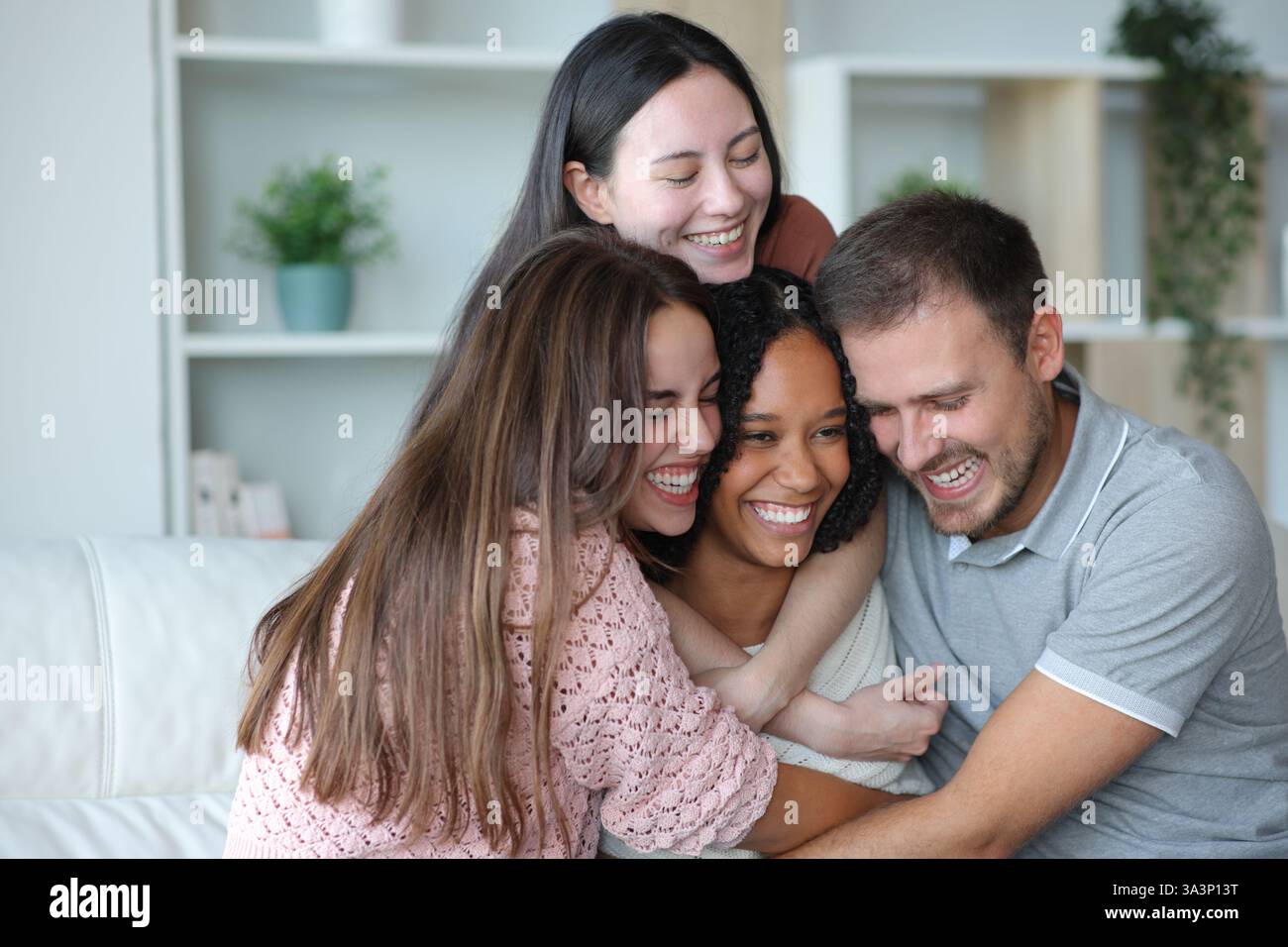 Happy group of best interracial friends hugging sitting on a couch at home Stock Photo