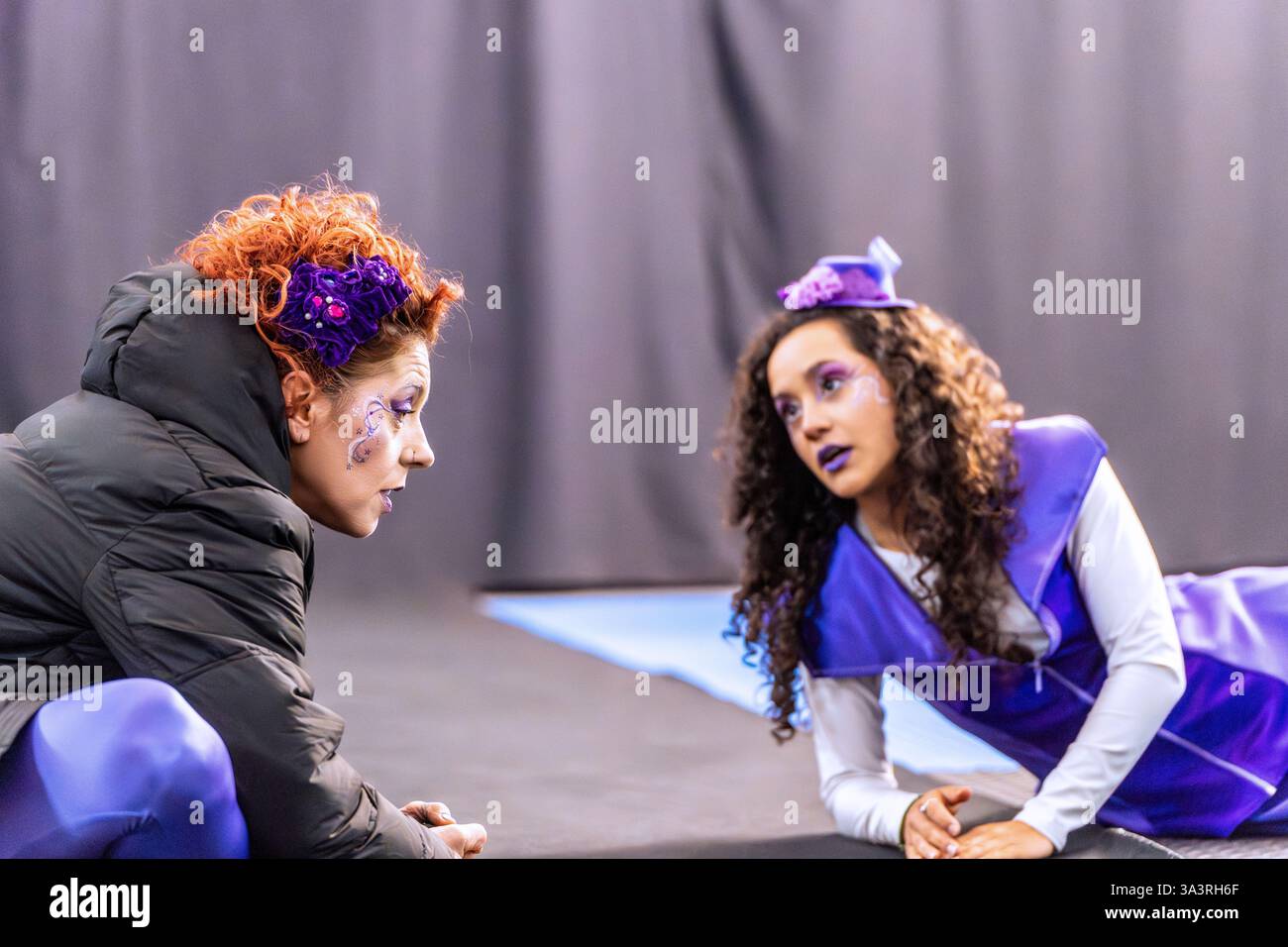 Two actresses wearing colorful costumes and makeup are rehearsing a ...