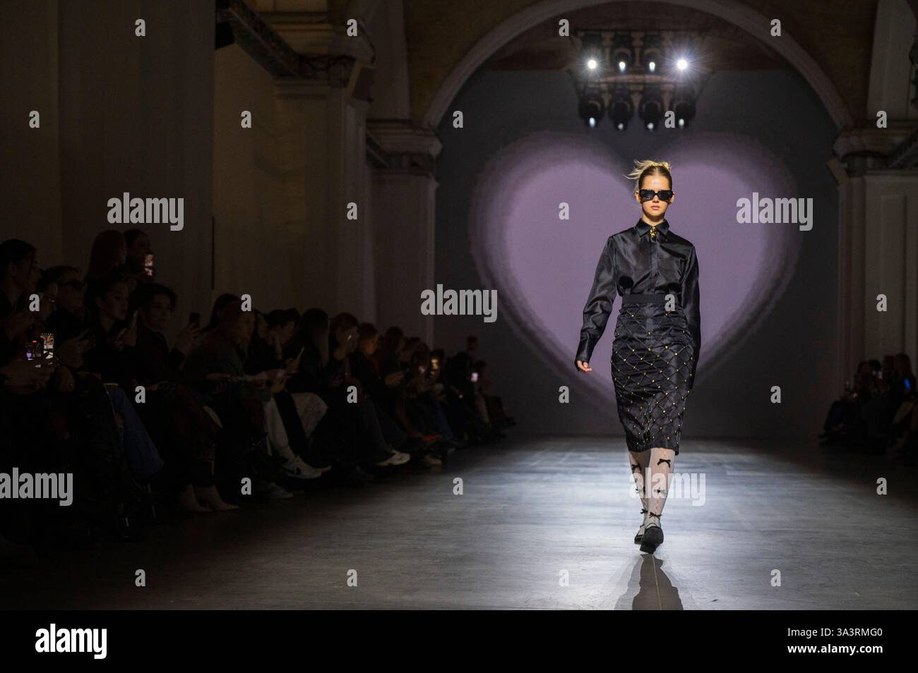 During Ukrainian Fashion Week FW25-26, a model confidently walks the runway in a sleek black ensemble, highlighted by a sophisticated silhouette and s Stock Photo