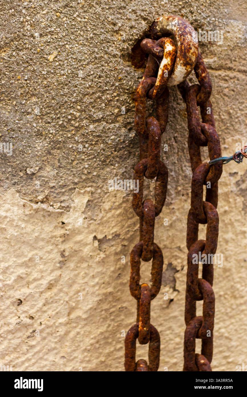 Old Rusty Chain Hanging on a Weathered Stone Wall Stock Photo
