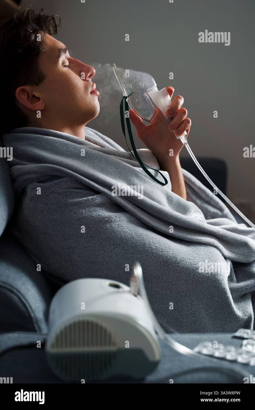 Man inhaling through oxygen mask for cough treatment. Using compressor ...