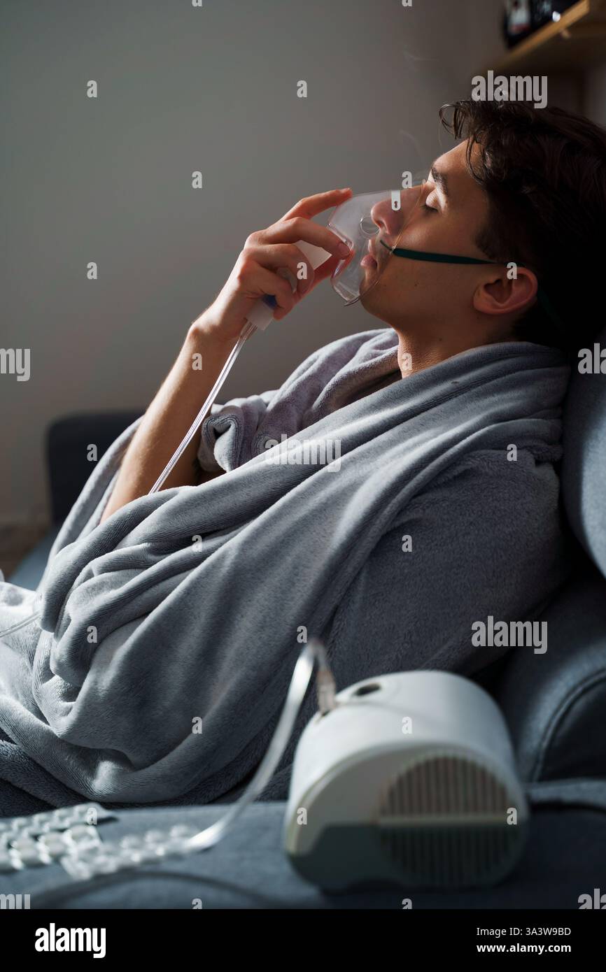 Man inhaling through oxygen mask for cough treatment. Using compressor ...