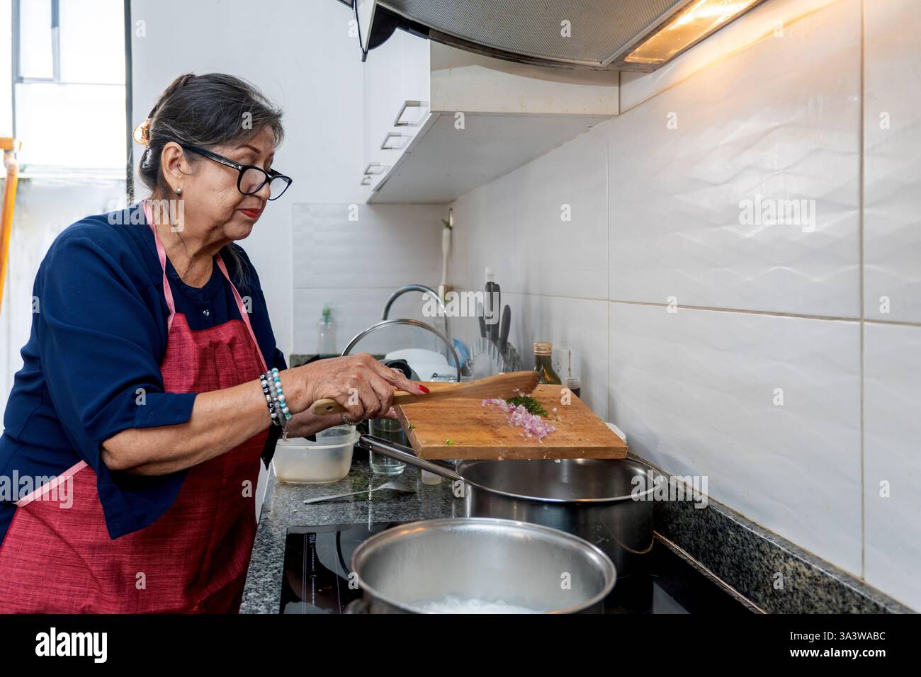 Elderly latin woman wearing an apron preparing ingredients on a cutting ...