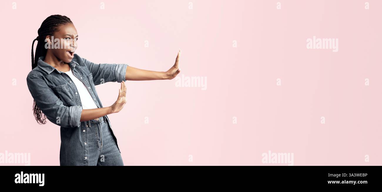 Woman expressing surprise in denim outfit against a light pink backdrop Stock Photo