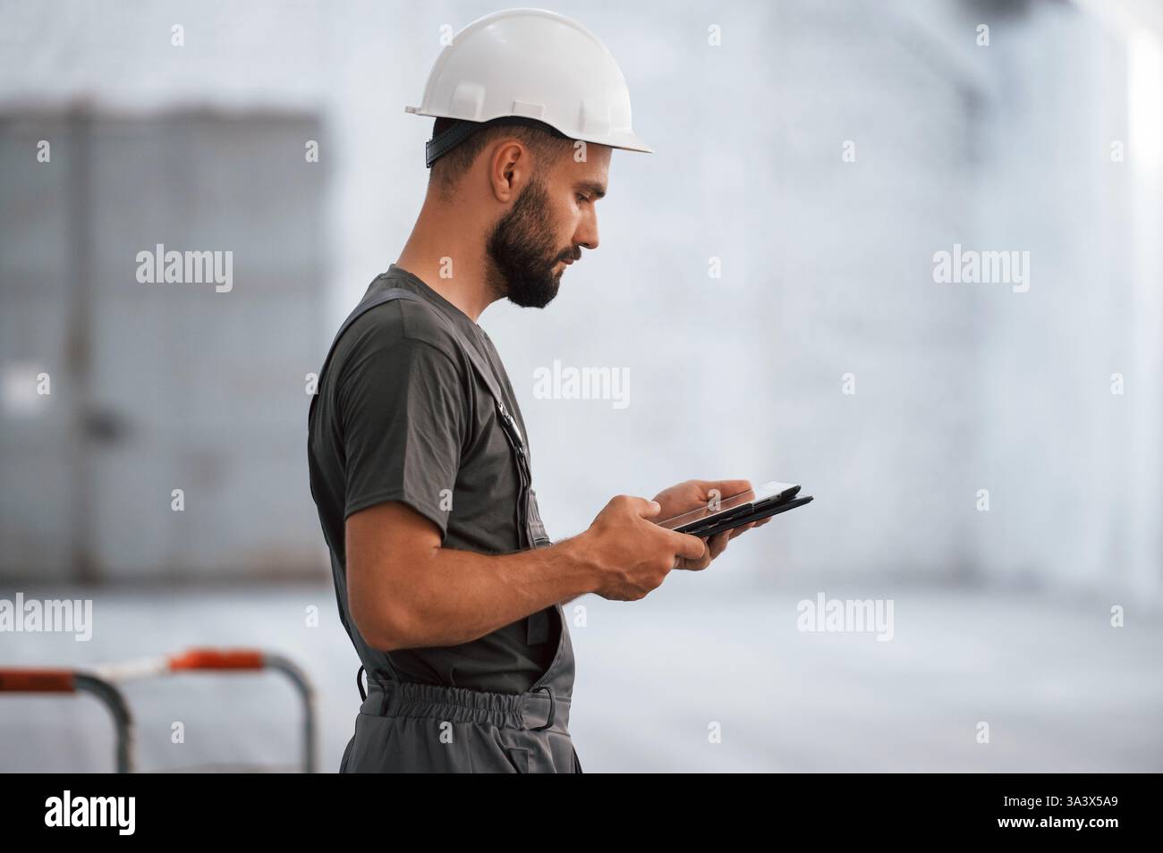 Side view, using digital tablet. Male worker is in the empty warehouse. Stock Photo