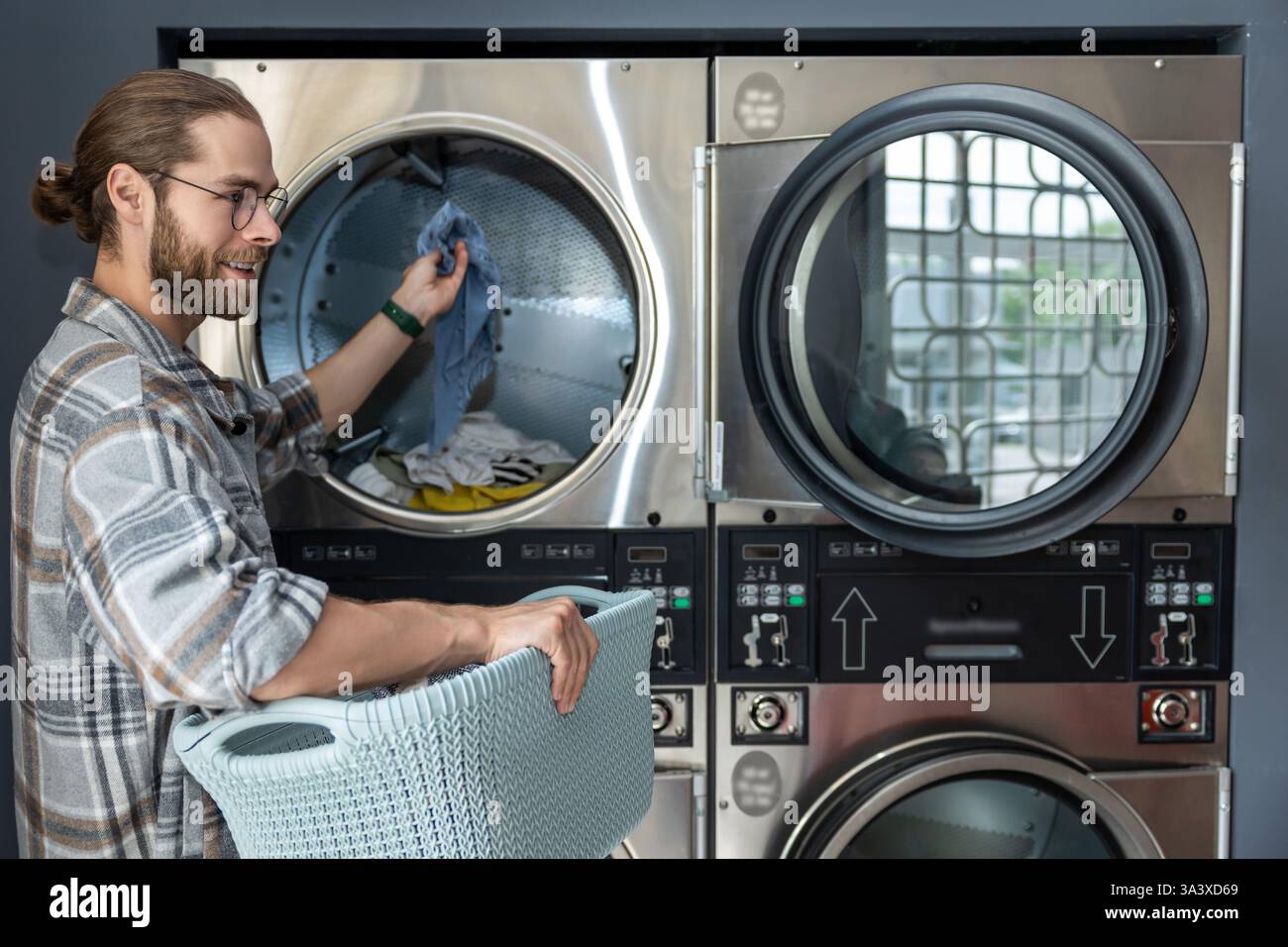 Washing While Machine Man in laundromat using commercial washing machine while completing his ...