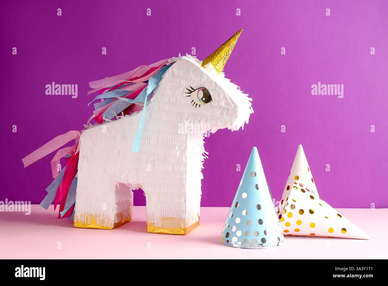 Bright pinata in shape of unicorn and party cones on color background ...