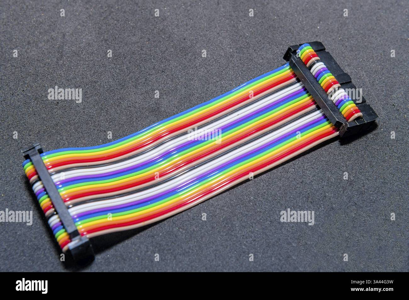 A rainbow-colored ribbon cable with connectors lying on a dark surface Stock Photo