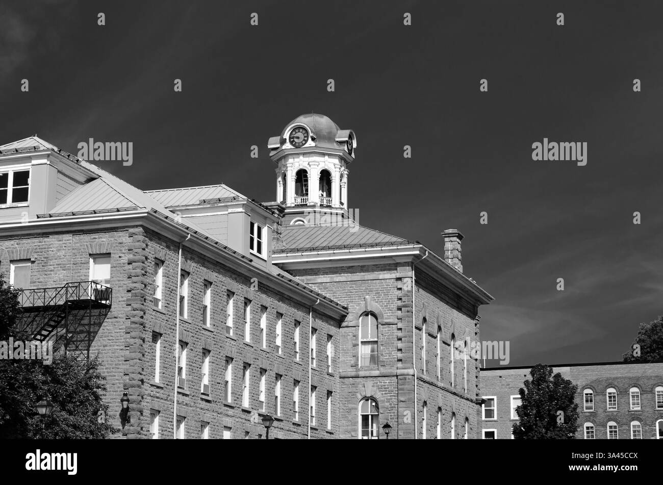 Black and white view of sunlit Brockville, Canada's city hall and clock tower against a dark sky backdrop. Stock Photo