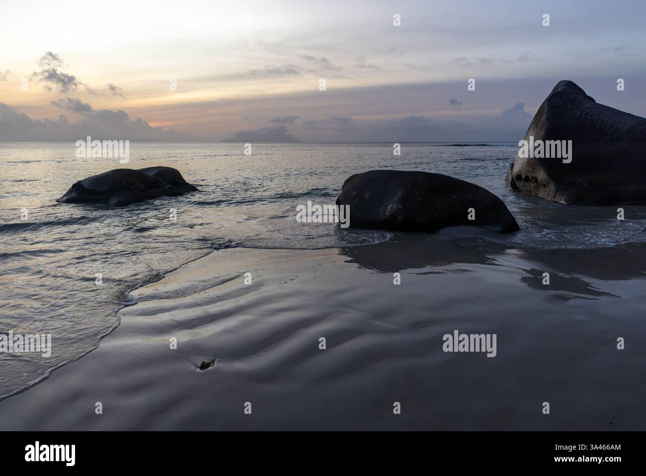 A peaceful beach scene featuring smooth sand, large scattered rocks ...