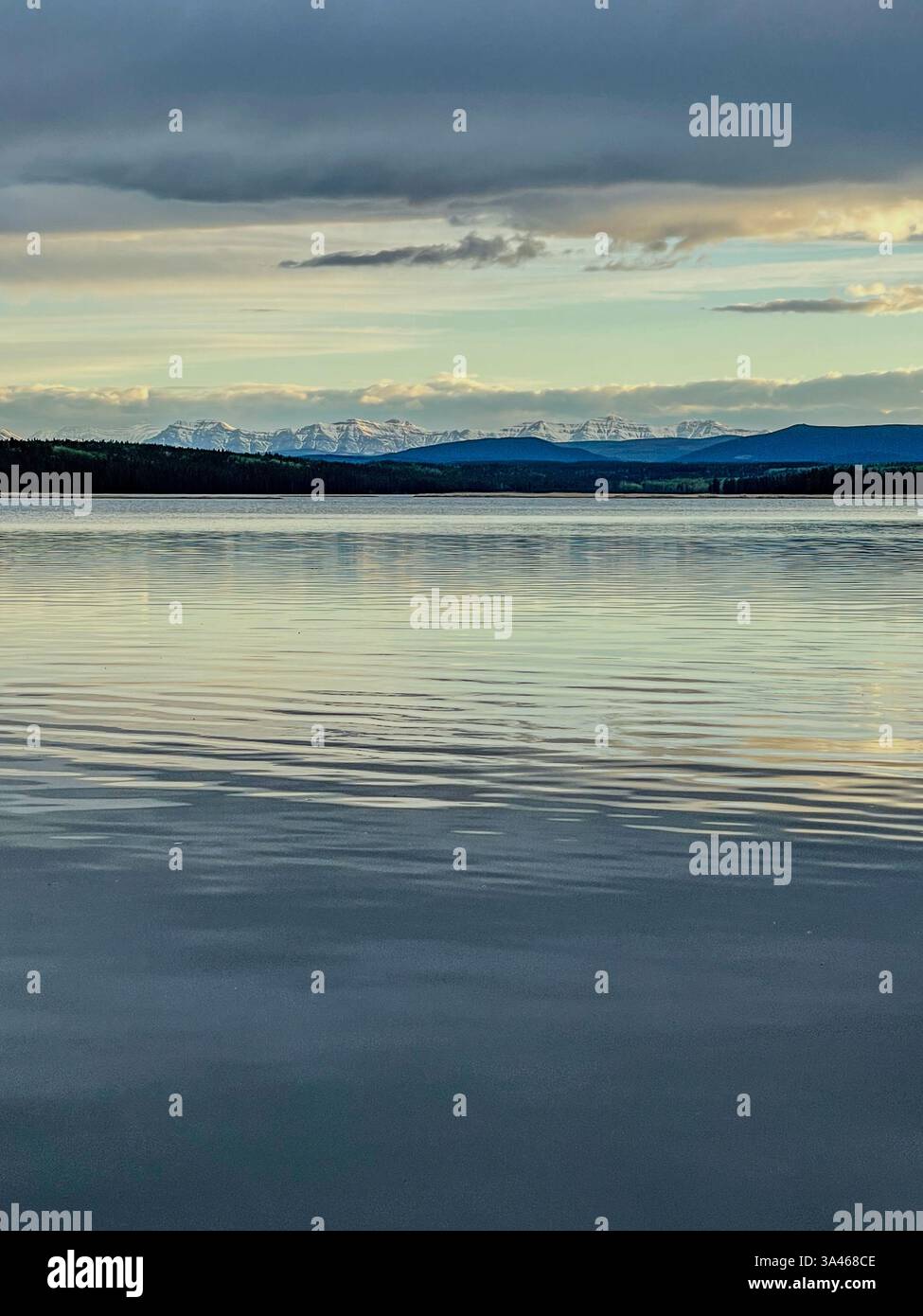 A calm lake reflecting distant mountains and clouds at sunset, with soft light and peaceful surroundings. The natural beauty of the scene is accentuat - Smartphone Captured Stock Image