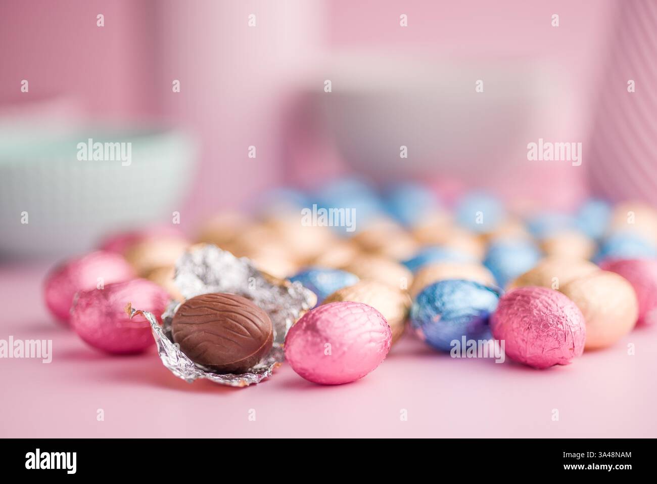 Chocolate easter eggs wrapped in multi colored foil on a pink background. Stock Photo
