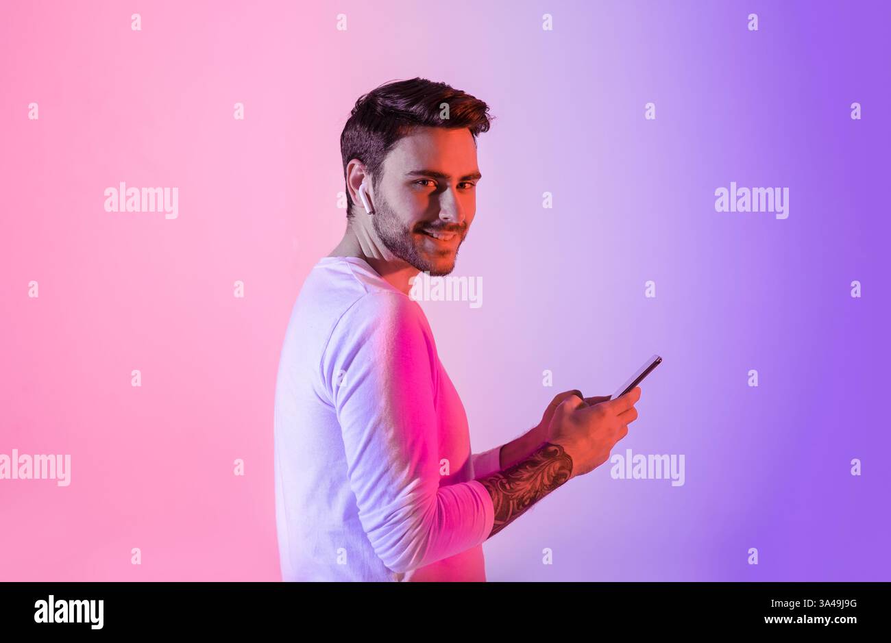 Young man smiling while using smartphone against colorful backdrop Stock Photo