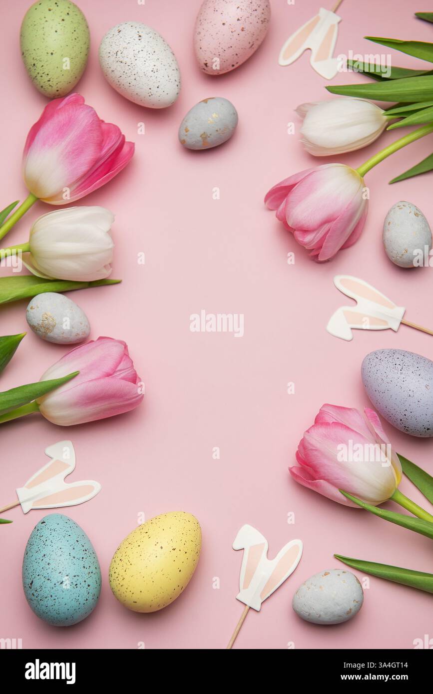 Easter eggs and pink and white tulips creating a frame on a pink ...