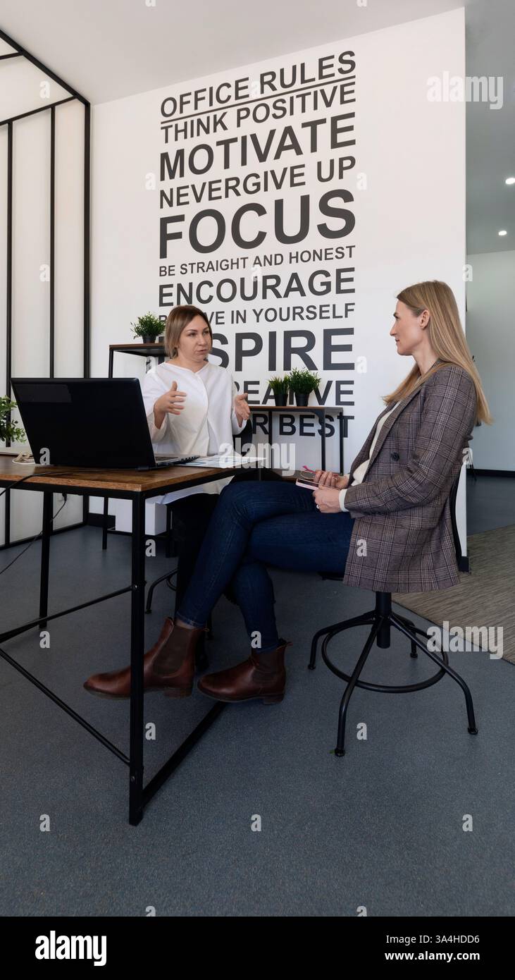 Engaging discussion between two women in a modern office setting focused on motivation and self-improvement strategies Stock Photo