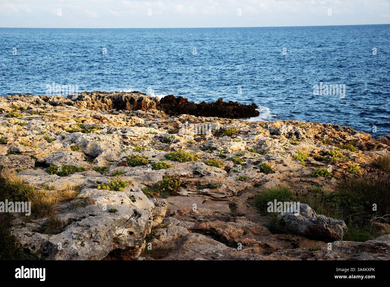 typical Menorca coast line with dark blue sea and jagged rocks with few ...