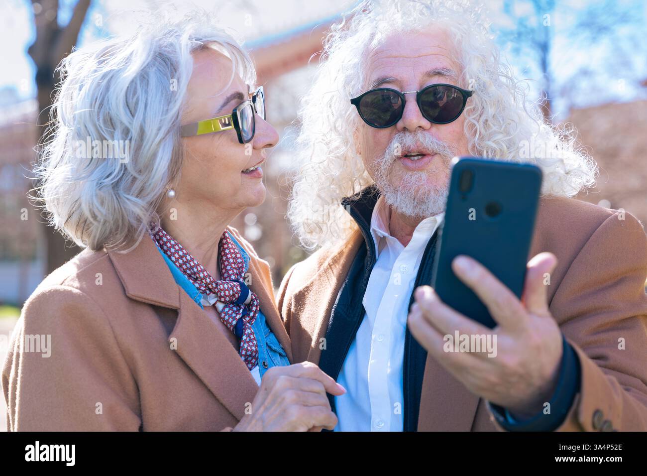 Senior couple using smartphone outdoors, enjoying technology and digital trends. Stock Photo