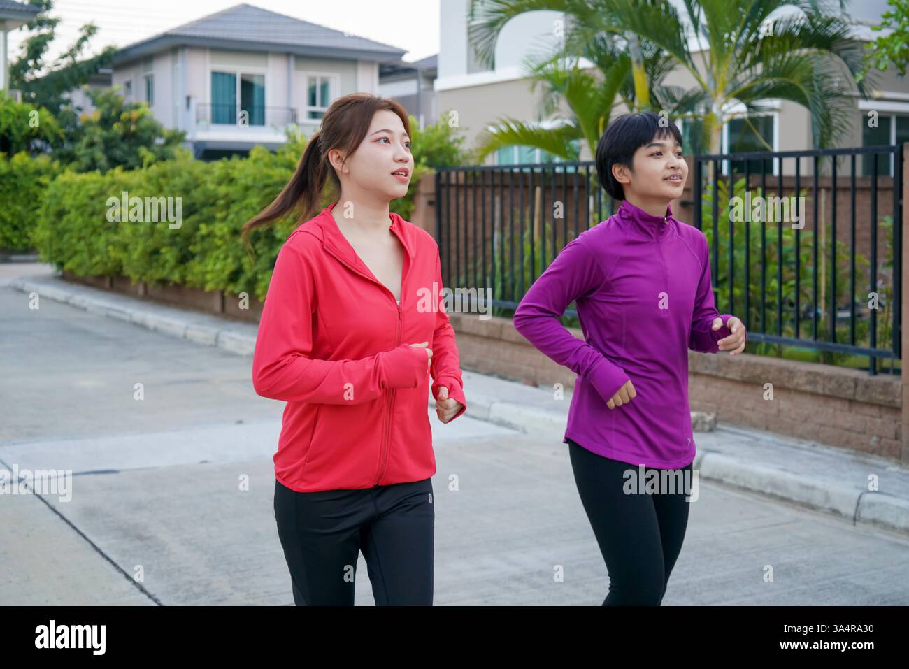 Side Jogging two asian friends jogging side by side in a quiet suburban area ...