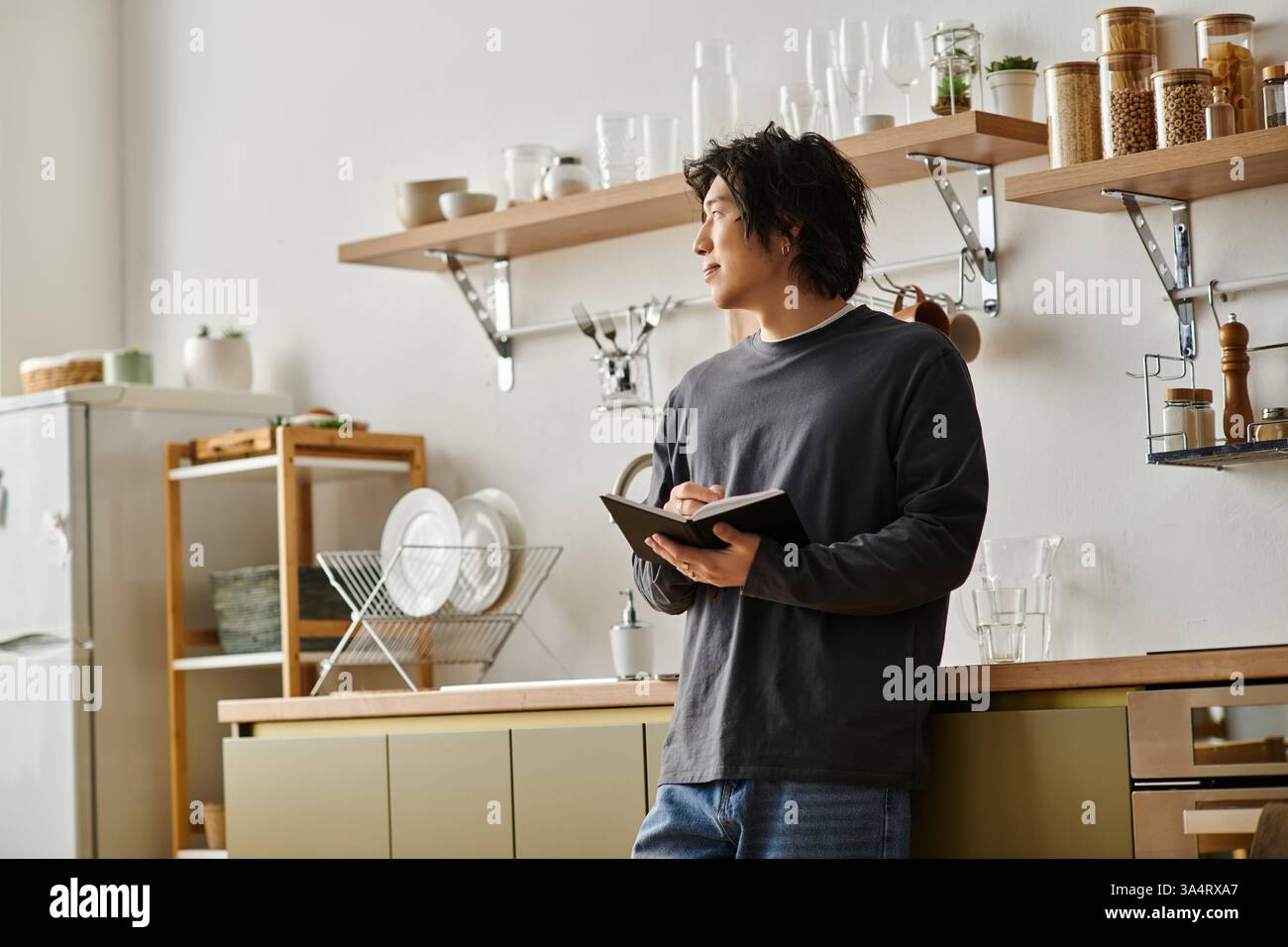 A focused young man studies online at home while taking notes in his notebook. Stock Photo