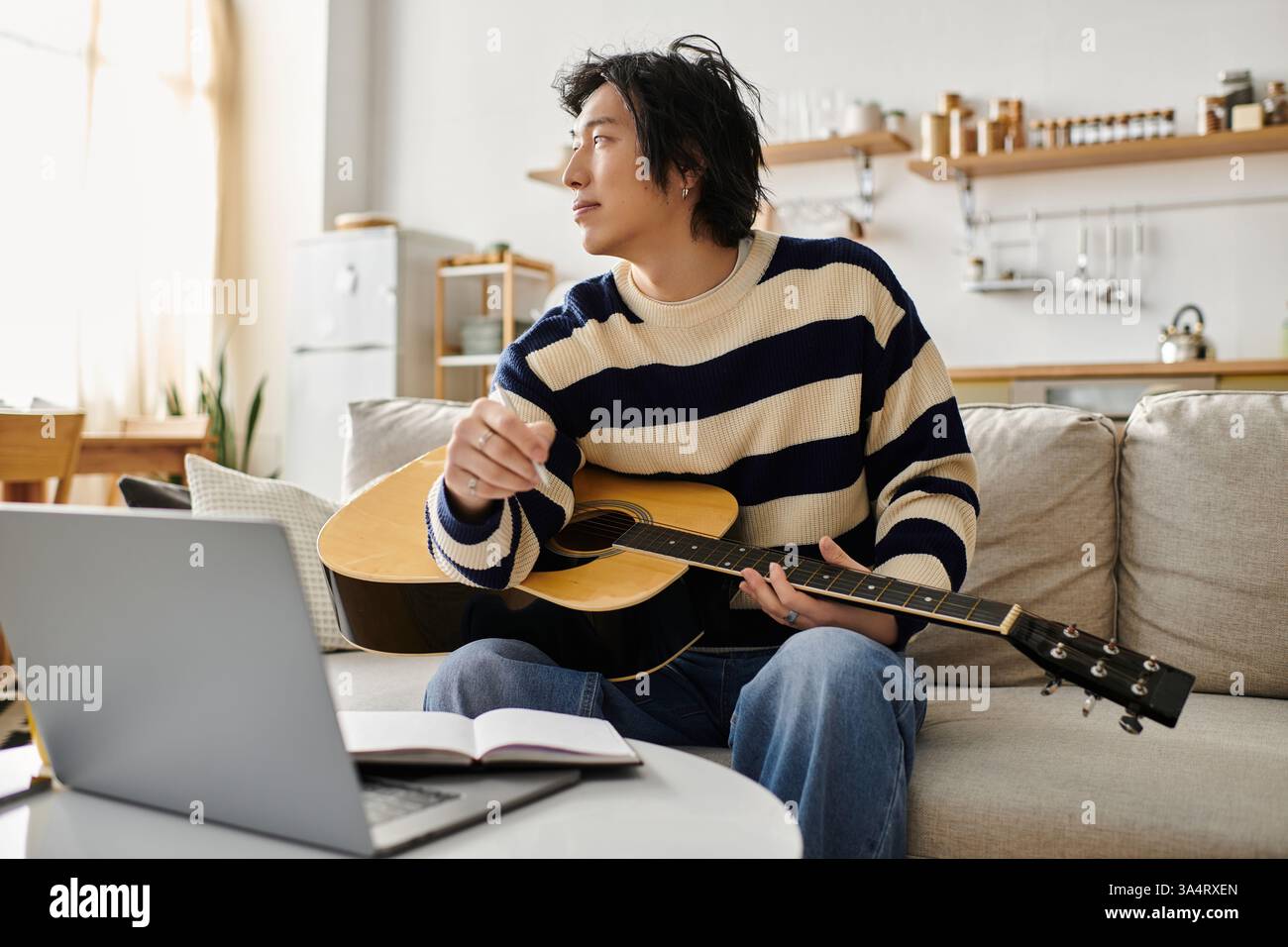 Handsome young man focuses on learning acoustic guitar while sitting comfortably at home. Stock Photo