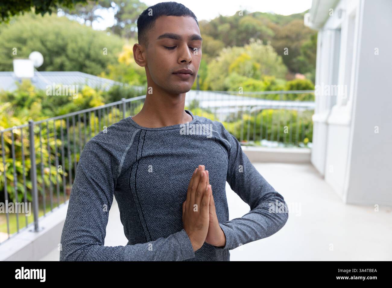Young man practicing yoga on balcony, meditating with hands in prayer position, copy space Stock Photo
