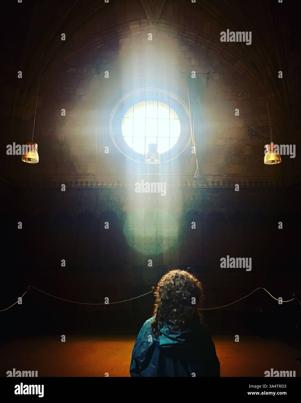 A woman watches sunlight forming a cross in a window in Santo Tomás monastery in Ávila, Castilla y Leon, Spain - Smartphone Captured Stock Image