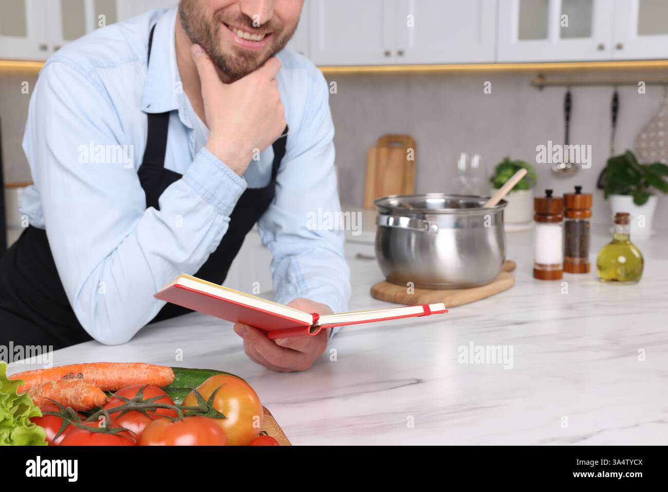 Man with recipe book at white marble table in kitchen, closeup Stock Photo