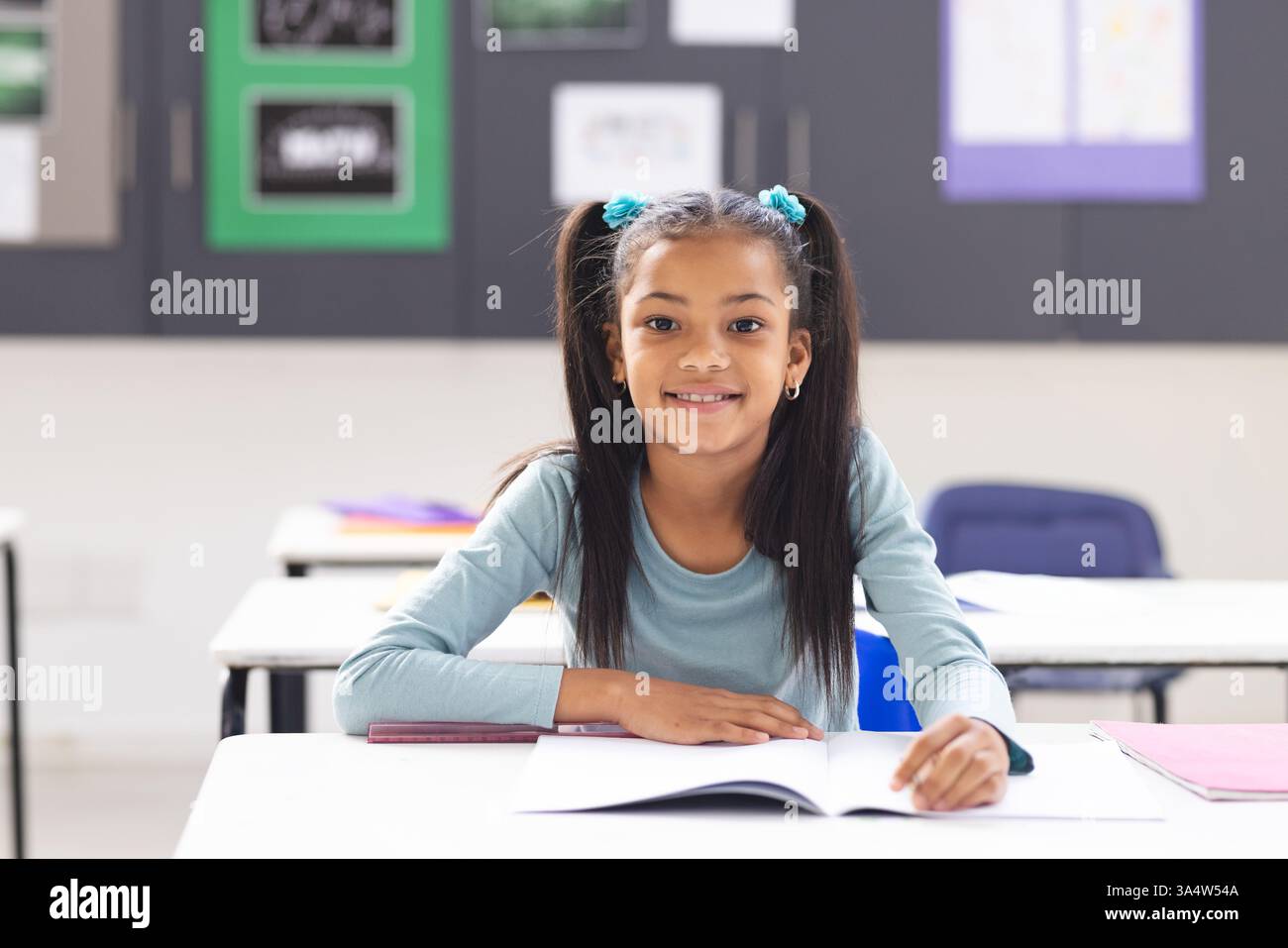 Smiling girl sitting at desk in classroom, ready to learn Stock Photo ...