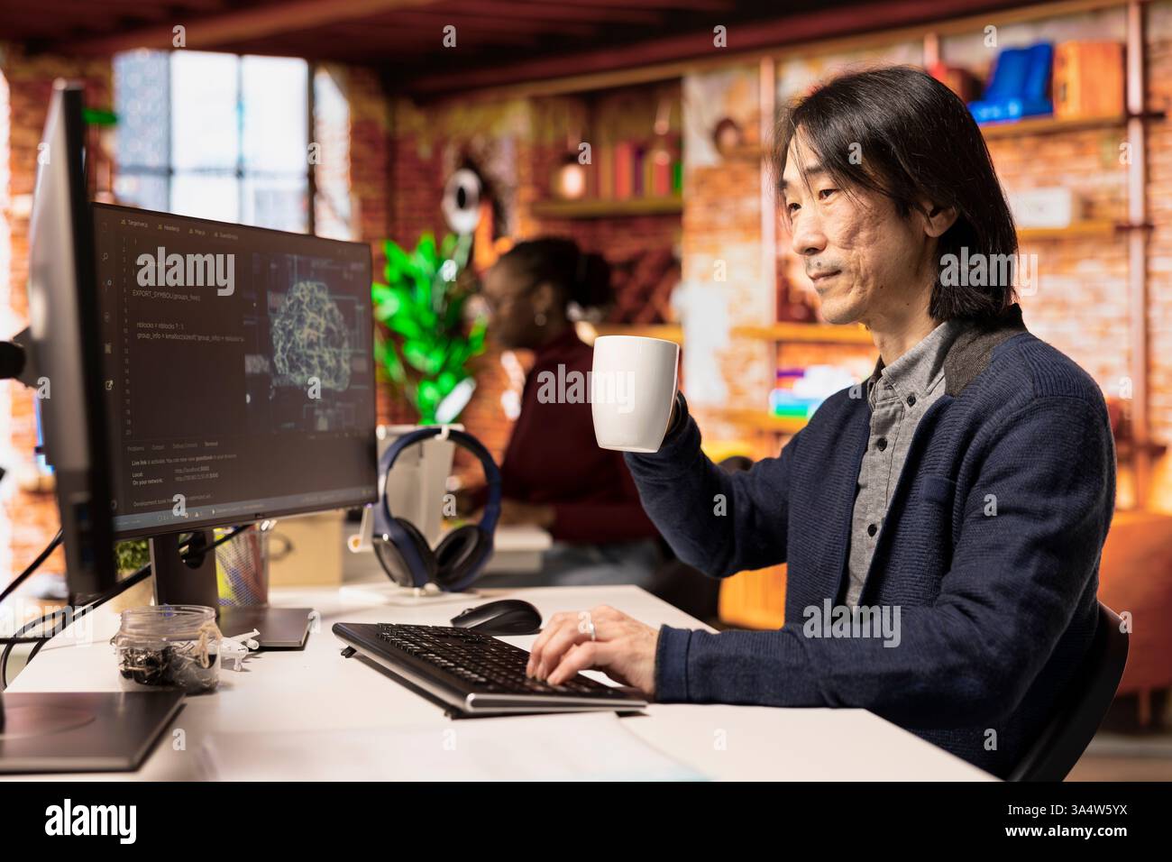 Senior programmer in artificial intelligence focused startup drinking coffee, coding and debugging applications. Experienced IT professional doing code testing and quality assurance, enjoying beverage Stock Photo