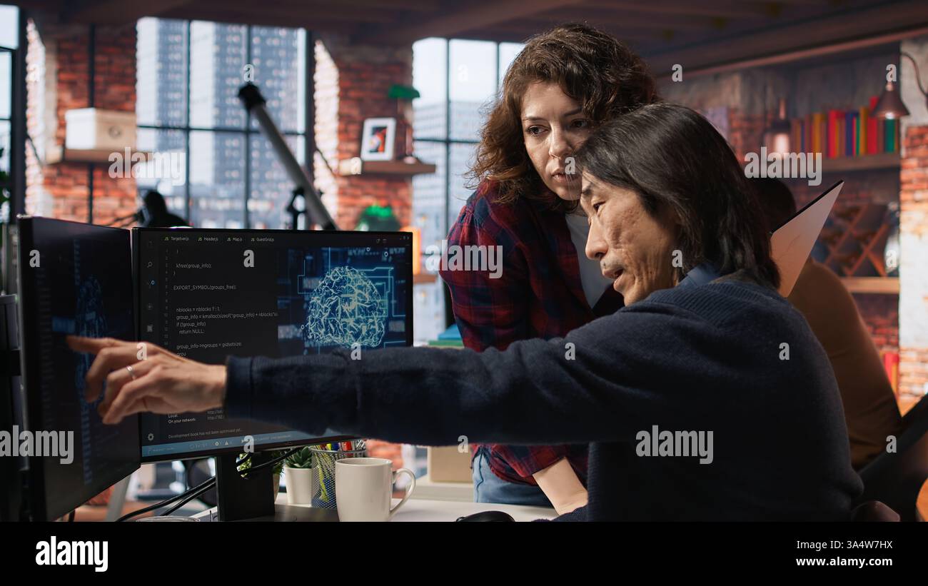 IT engineers cooperating in AI focused startup, debugging applications, crosschecking between PC and laptop. Coworkers doing code testing and quality assurance on devices, camera A Stock Photo