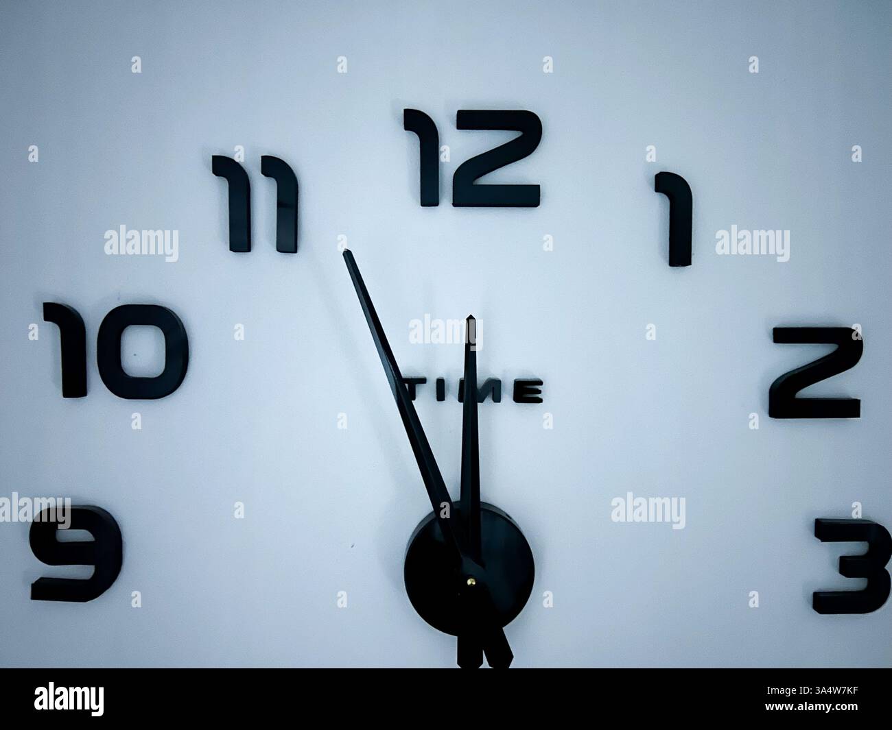 A minimalist wall clock with black hands and numbers on a white background, showing 5 minutes to 12 o’clock, symbolizing urgency, countdown. - Smartphone Captured Stock Image