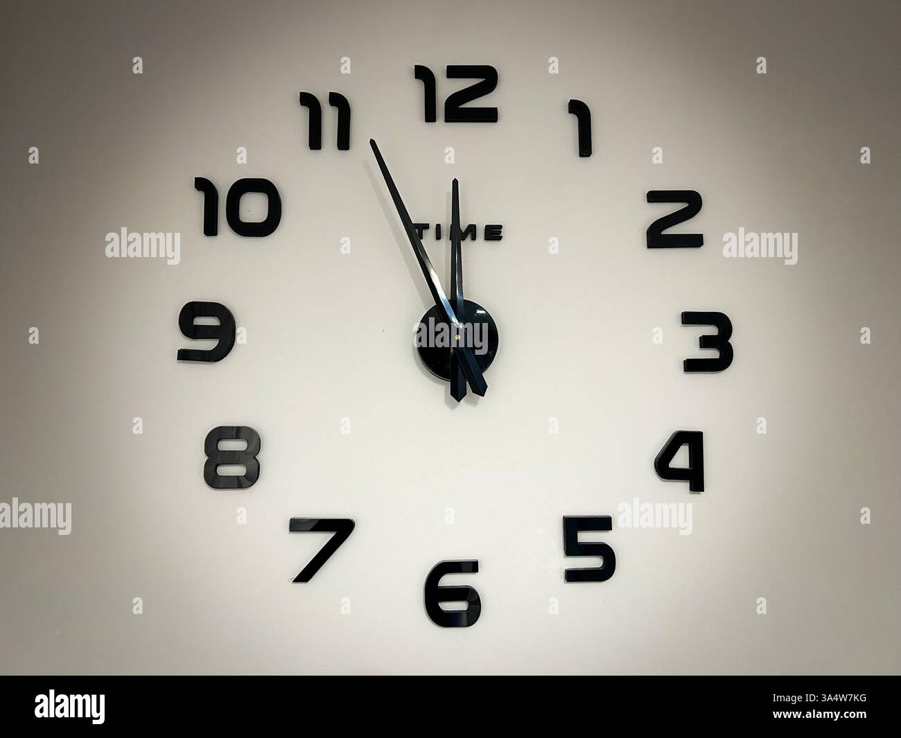 A minimalist wall clock with black hands and numbers on a white background, showing 5 minutes to 12 o’clock, symbolizing urgency, countdown. - Smartphone Captured Stock Image