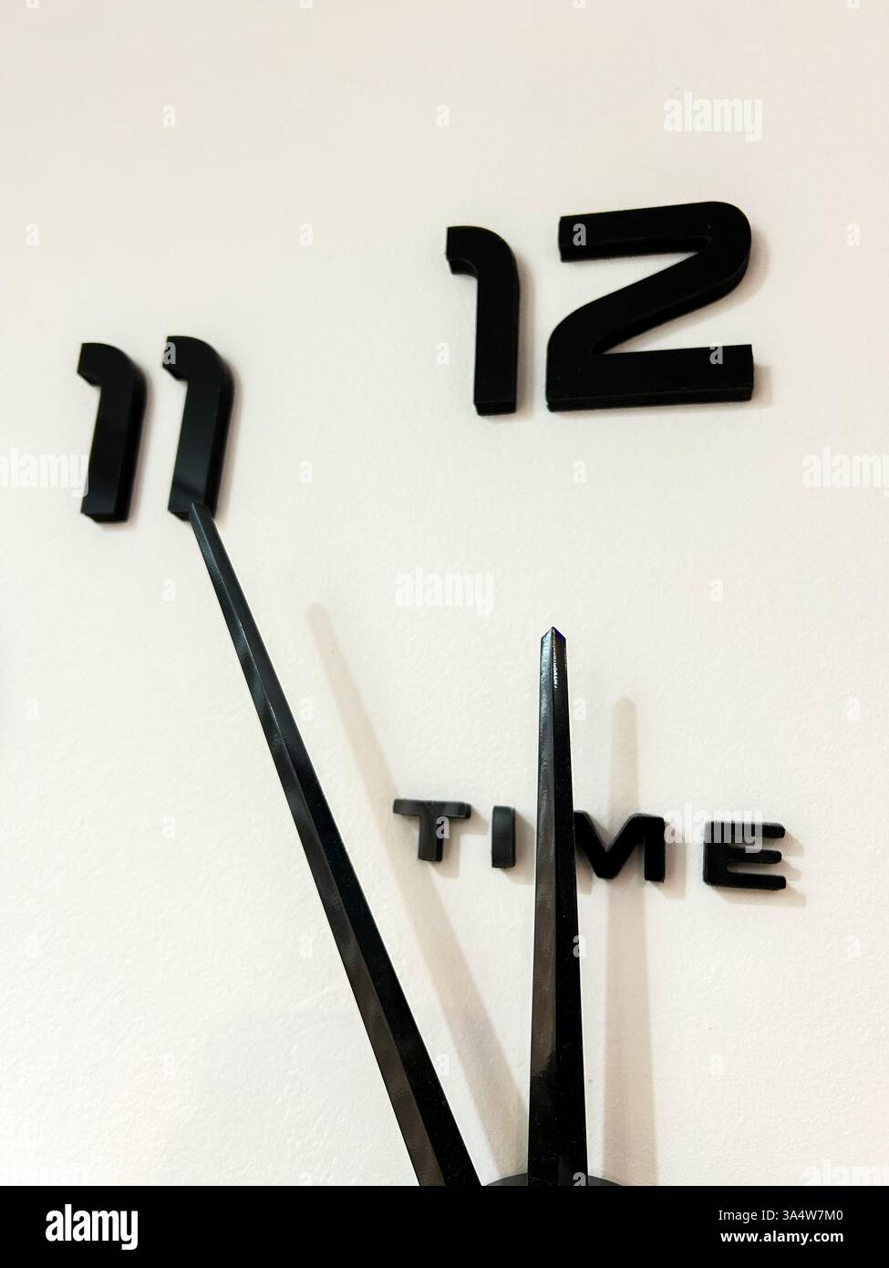 A minimalist wall clock with black hands and numbers on a white background, showing 5 minutes to 12 o’clock, symbolizing urgency, countdown. - Smartphone Captured Stock Image