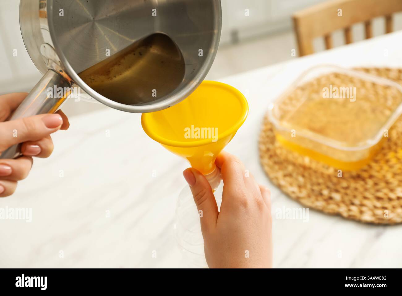 Woman pouring used cooking oil into bottle through funnel in kitchen ...