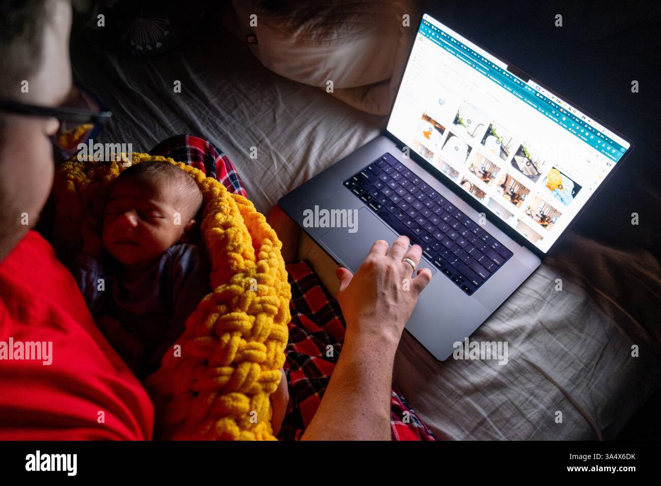 Father Holding Baby While Using Laptop in Dim Light Stock Photo