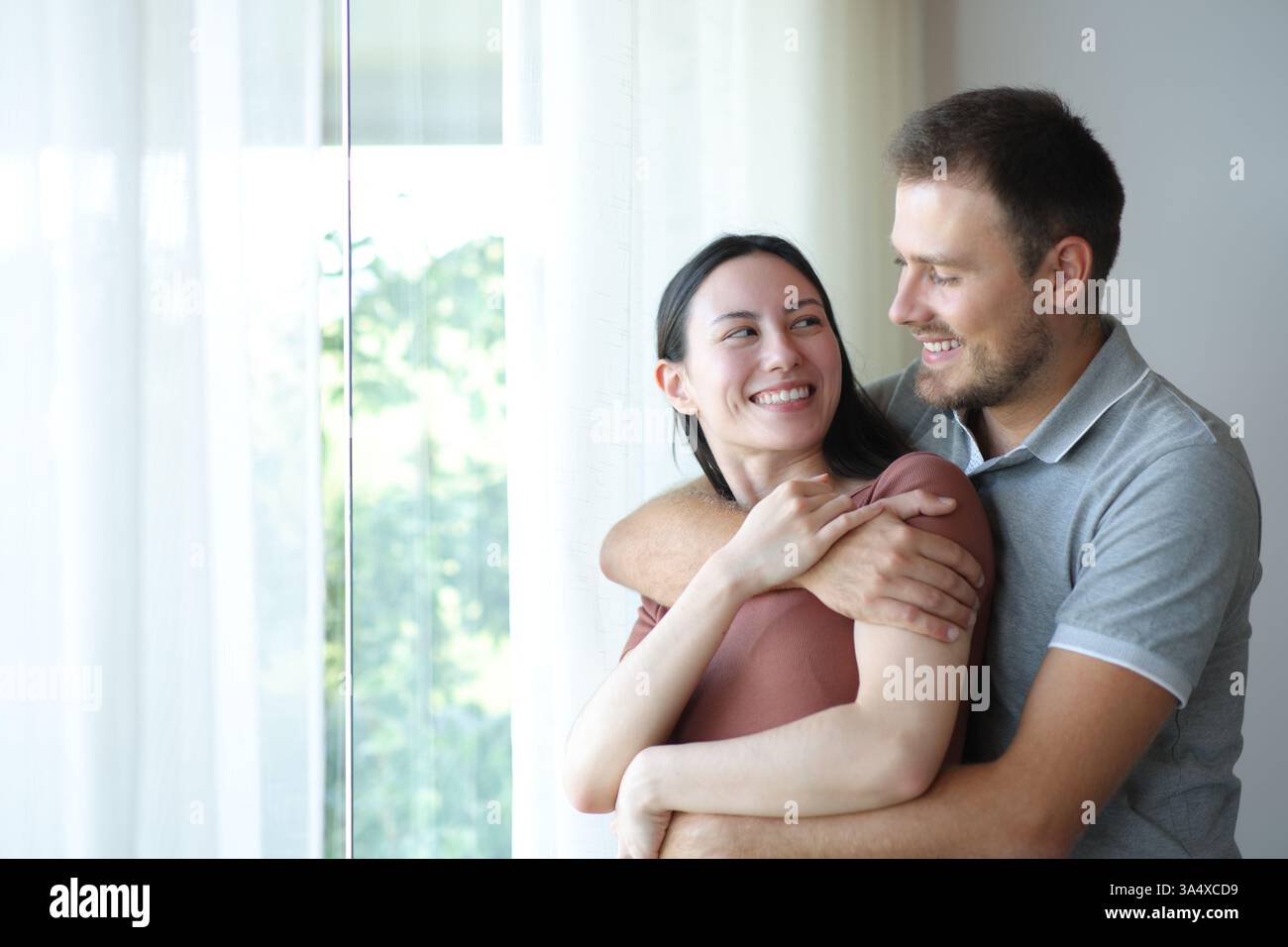 Happy interracial couple in love looking each other standing and hugging at home Stock Photo