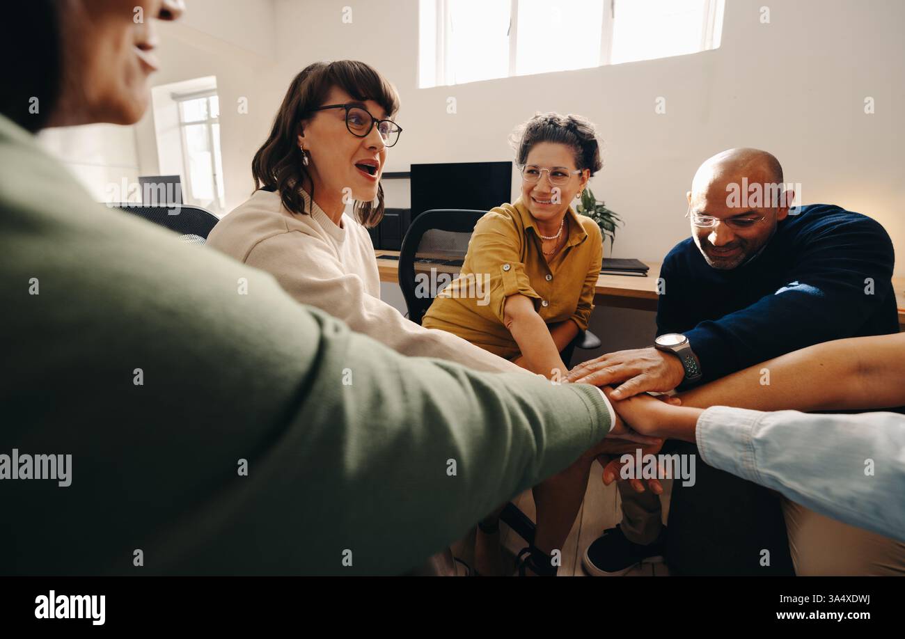 A team engaged in a collaborative discussion, showing unity and enthusiasm by joining hands together. The image reflects a professional work environme Stock Photo
