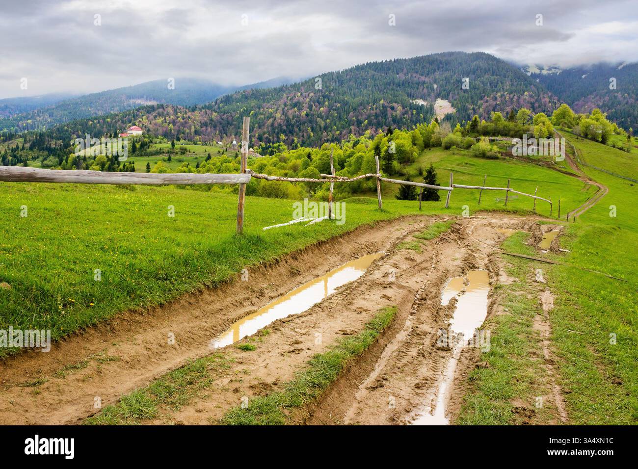 countryside mountain landscape in spring. green nature with cloudy sky. beautiful view with fence along the path through hill in the rain for tourism. Stock Photo