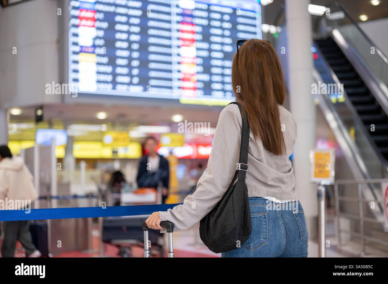 An attractive Asian female traveler is standing in front of a boarding time monitor in the airport, checking her flight boarding time. people and tran Stock Photo
