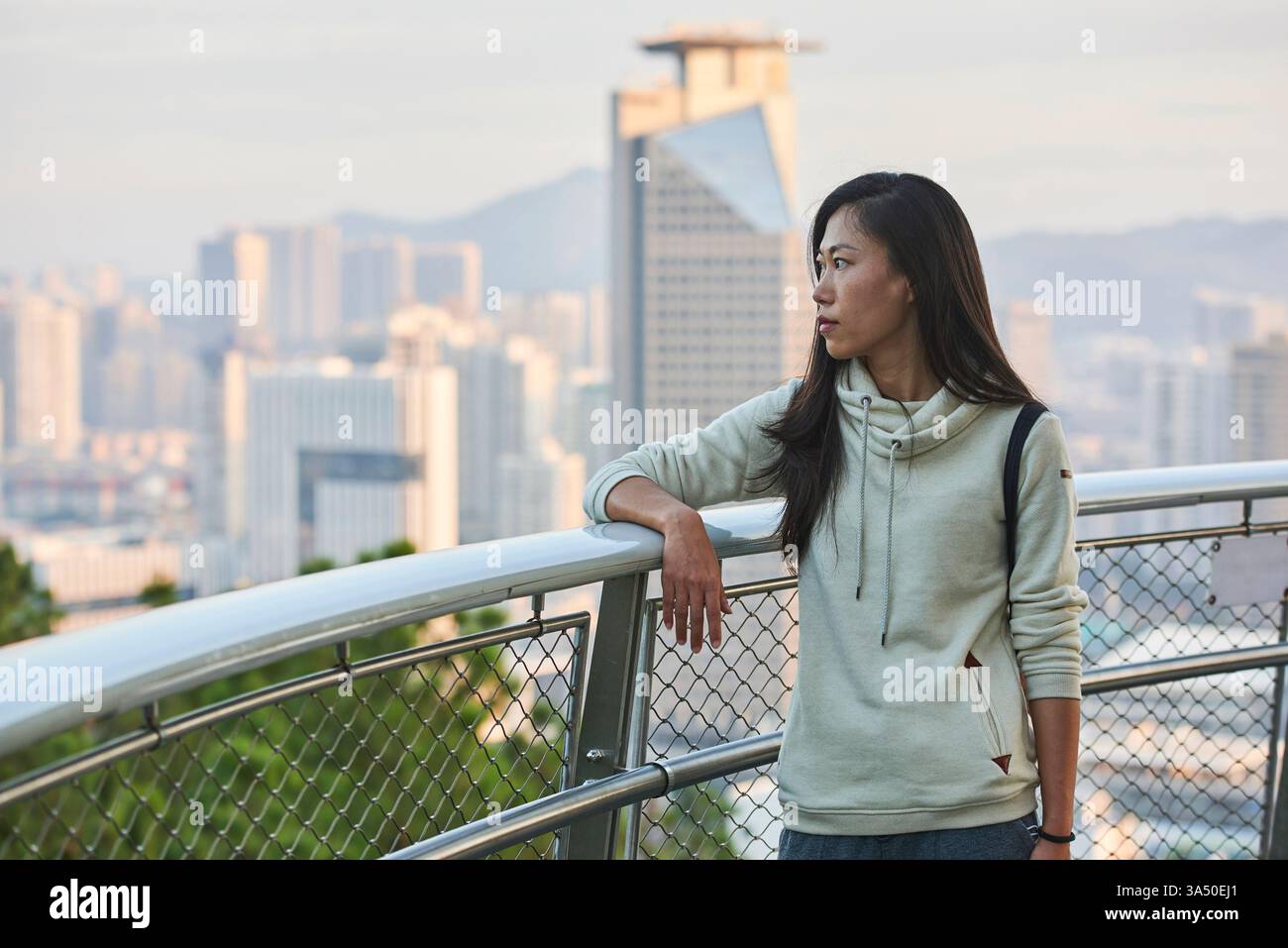Asian woman standing and leaning on metal railings looking away Stock ...