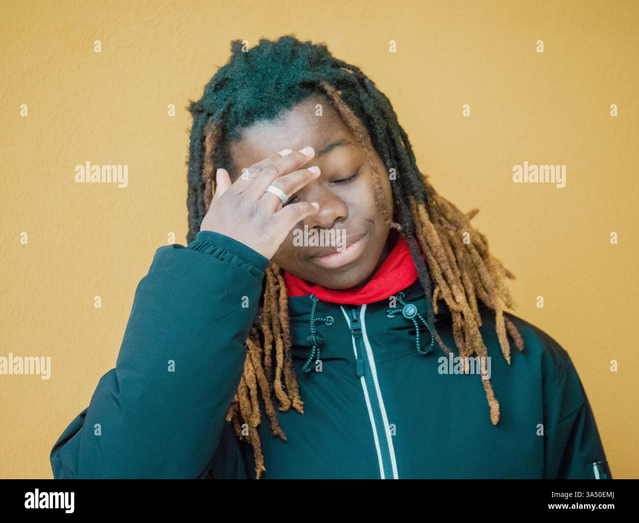 Serious young Black female with dreadlocks touching face standing with ...
