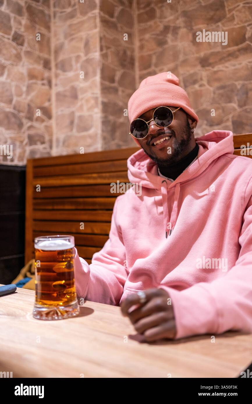 Vertical photo of a stylish african young man drinking beer in a bar ...