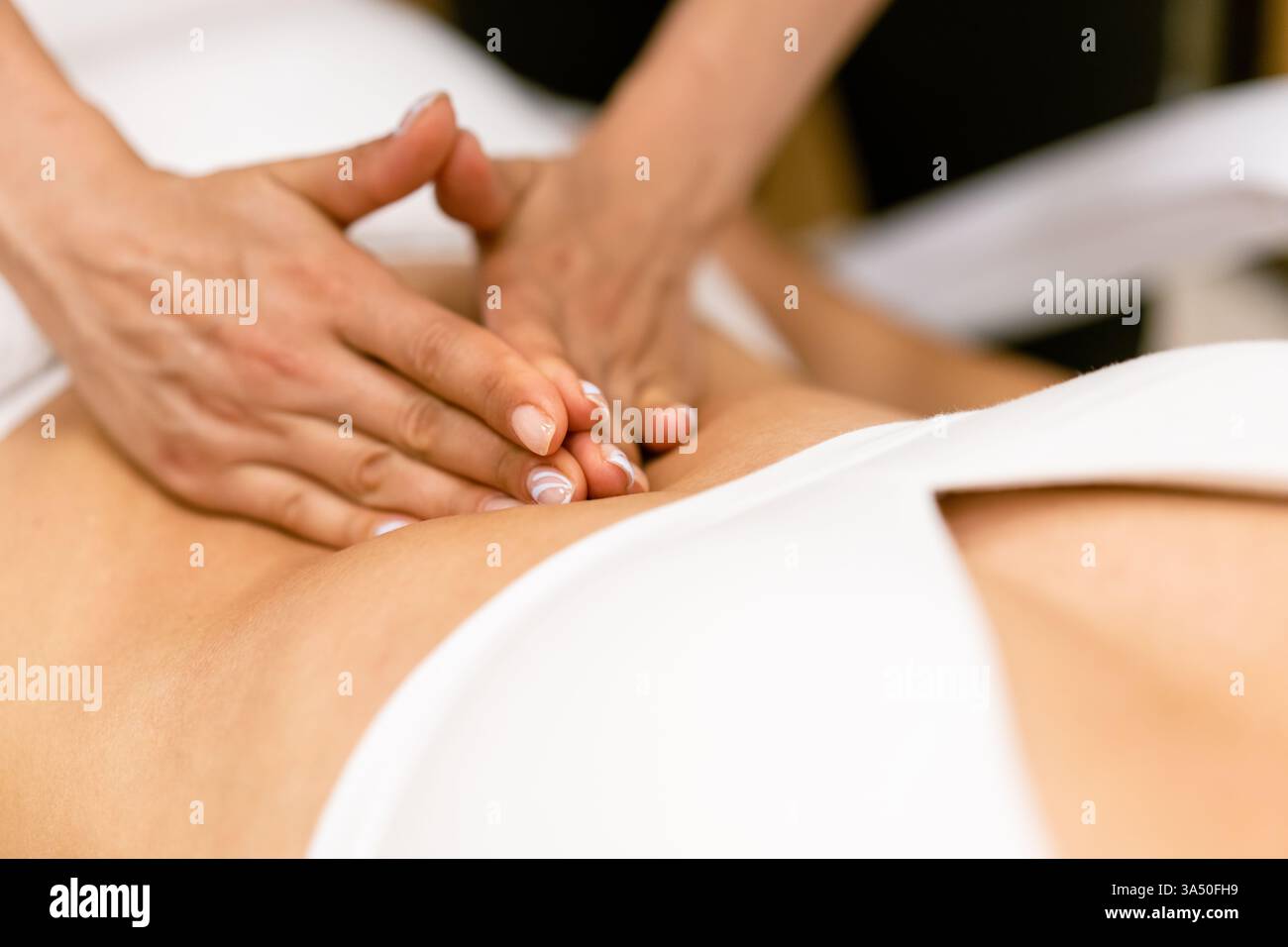 Hands of Middle Eastern female massage therapist massaging the belly of caucasian female client in spa Stock Photo