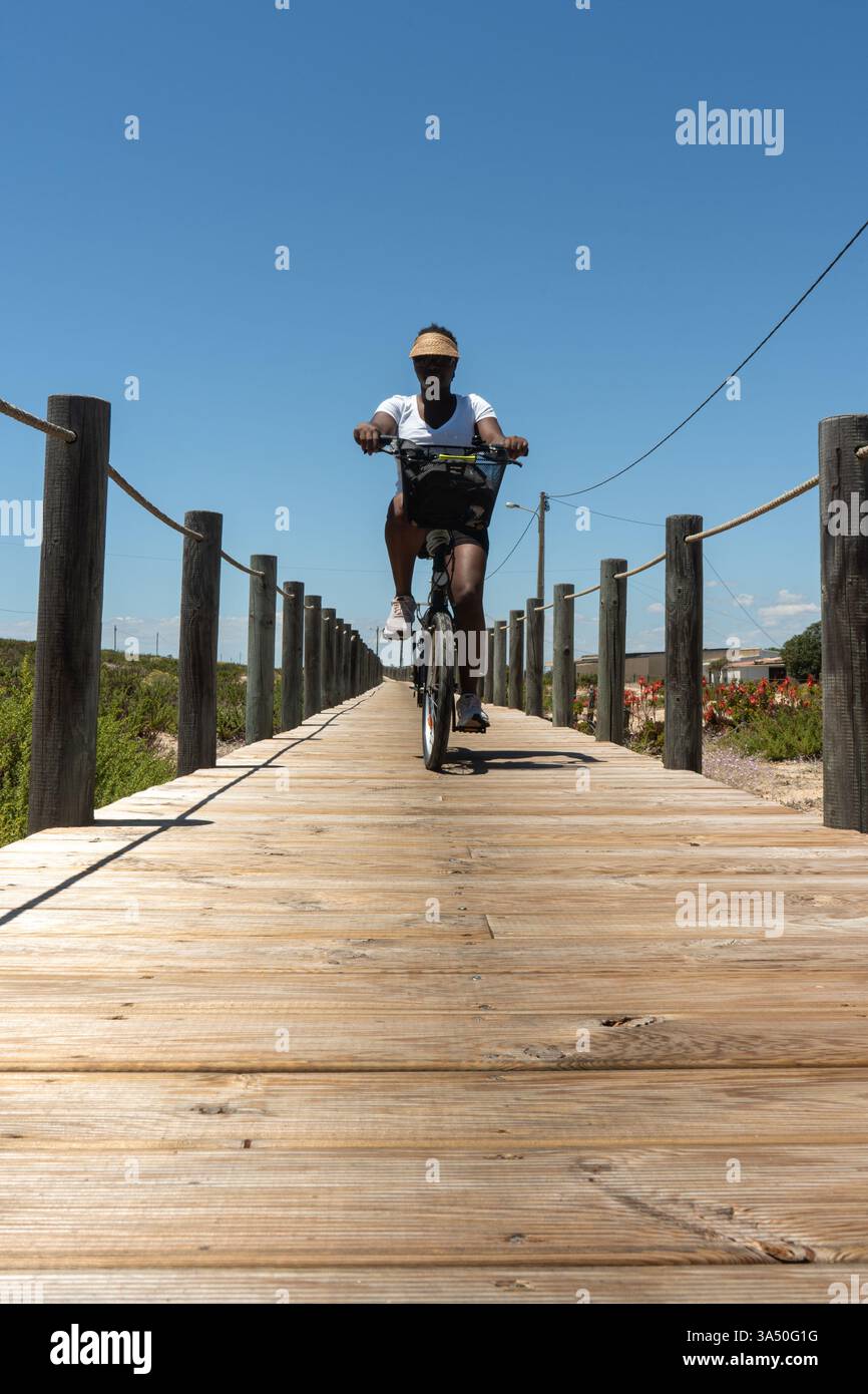 Black woman rides a bicycle along a sunlit walkway enjoying an outdoor ...