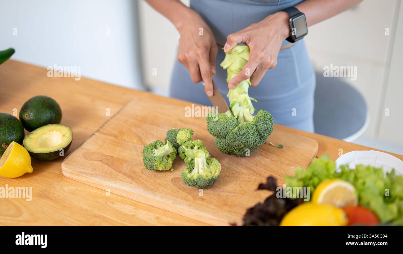 Close-up of a healthy, fit woman in gym clothes chopping broccoli on a ...