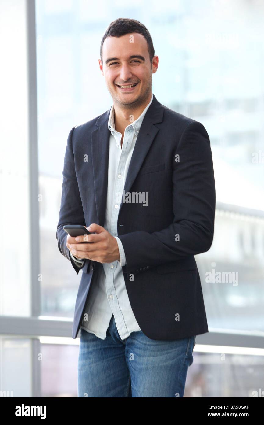 Cheerful Hispanic businessman using smartphone standing in glass building during daytime Stock Photo