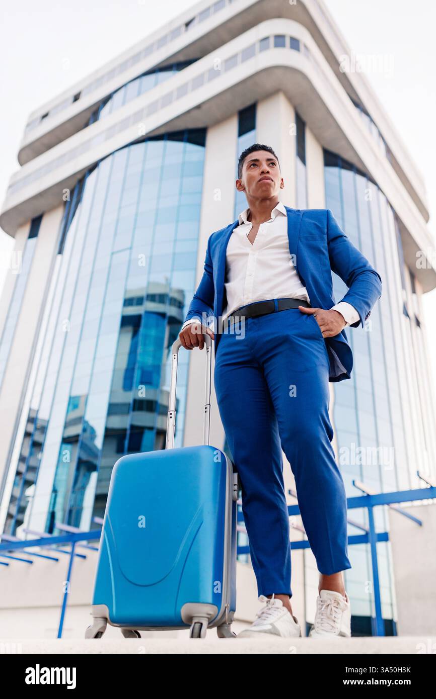 Hispanic male in business suit standing near suitcase on street Stock Photo